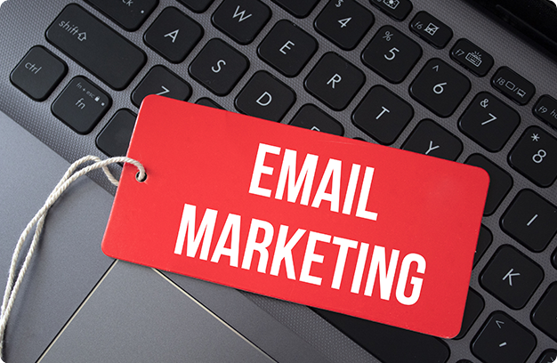 The words ''Email Marketing'' written on a piece of red paper with a laptop on the background