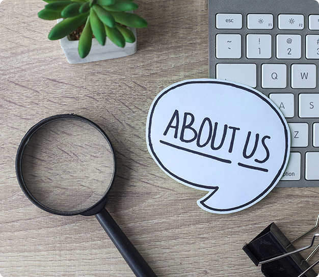 About Us written on white paper on a table with a keyboard, magnifying glass, and cactus