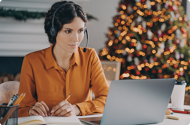 A girl with a headset sits in front of a laptop, writing in her notebook